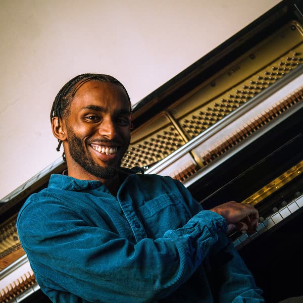 Judah laughing at an upright piano, turned towards the camera