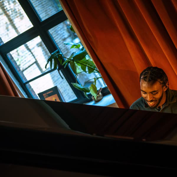 Judah smiling at a grand piano by a window with red curtains