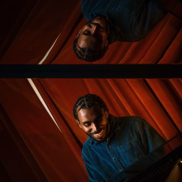 Judah reflected in the raised lid of a grand piano, red curtains behind