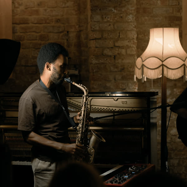 Judah playing saxophone under a fringed lamp, a guitarist beside him